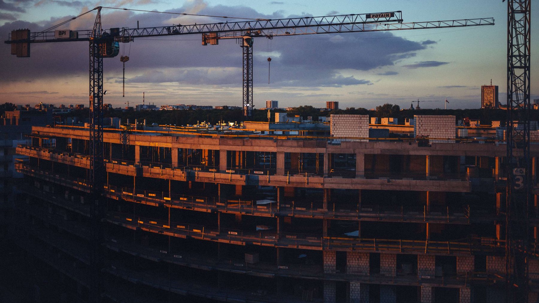 Building under construction at dusk with cranes