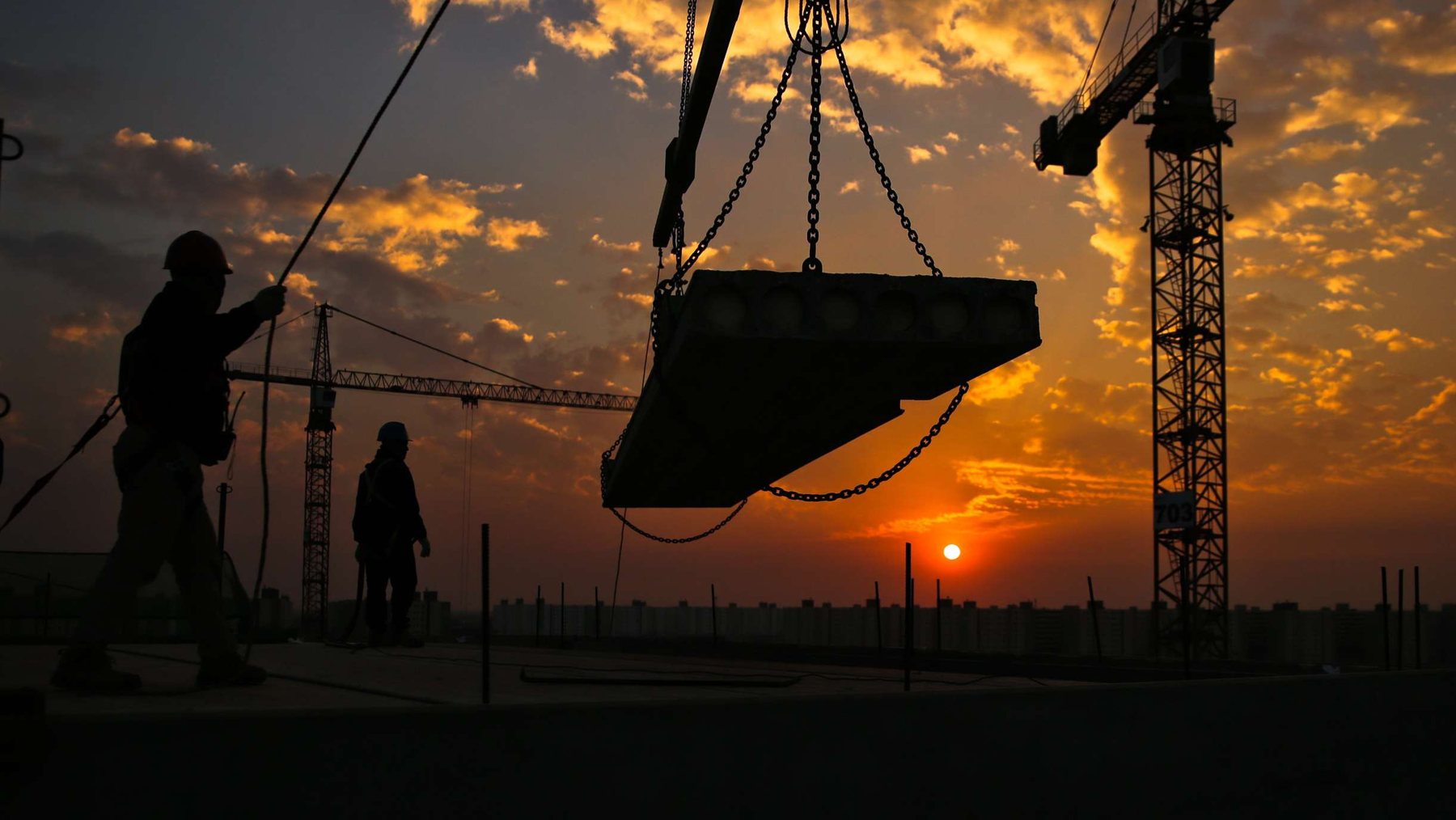 Construction crane and workers silhouetted at sunset
